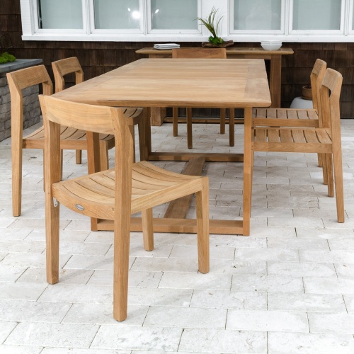 70498 Horizon Side Chair Dining Set on concrete patio a teak table with 2 stacks of white plates and bowls plant against wood shingle house with large windows in background